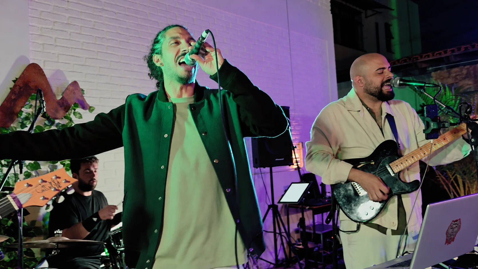 Músicos em apresentação ao vivo sob luzes verdes e roxas